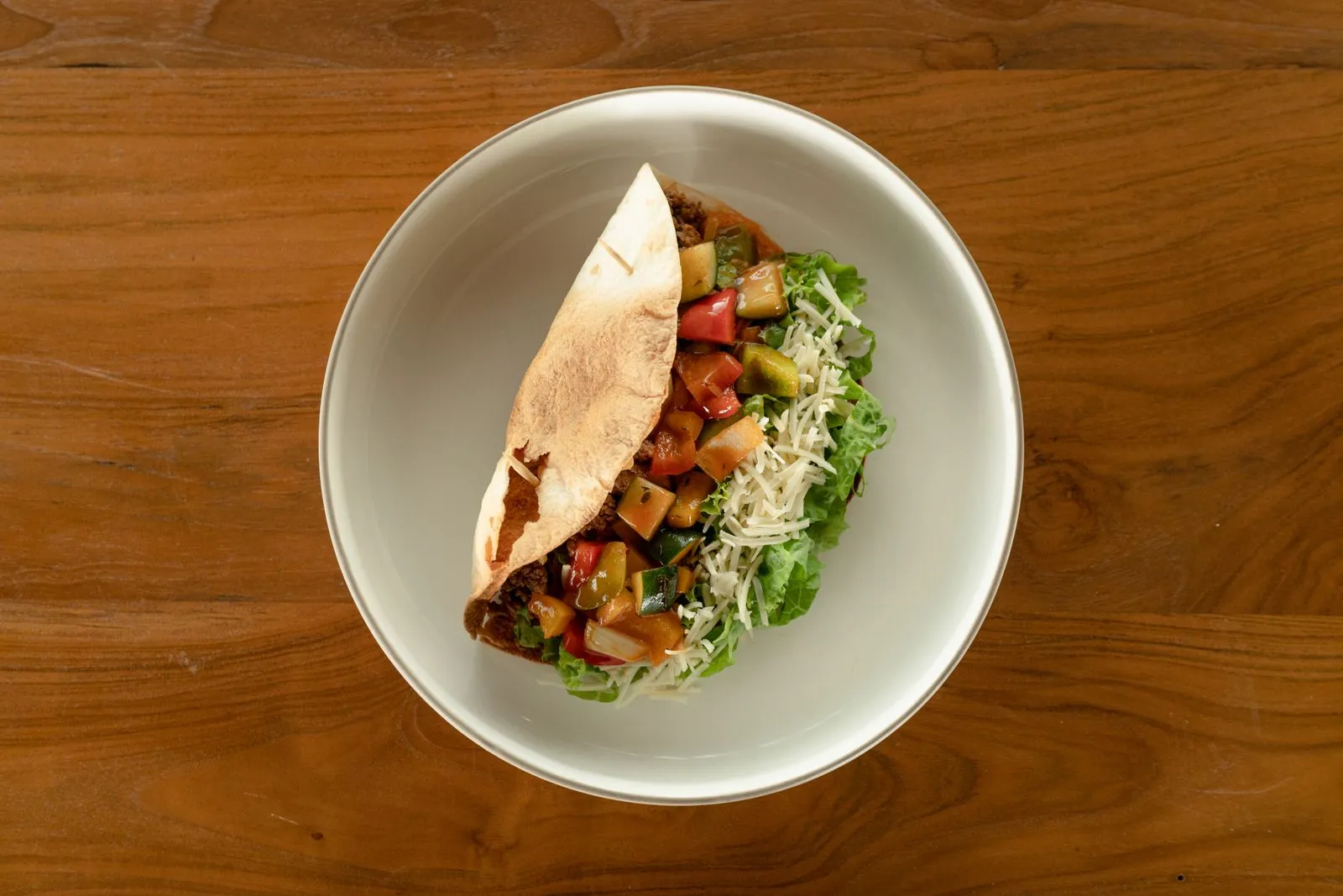 Top view of a fresh Mediterranean salad with pita and salsa on a wooden surface.